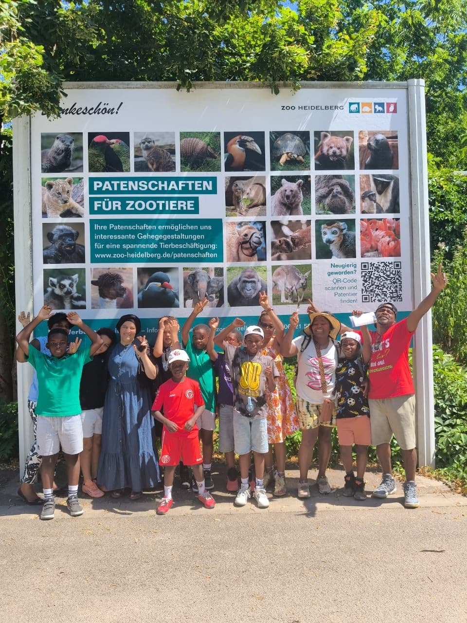 Kinder und Eltern von Makala Mboa e.V. vor der Patenschaftstafel für Zootiere beim Lehrausflug in den Zoo Heidelberg.